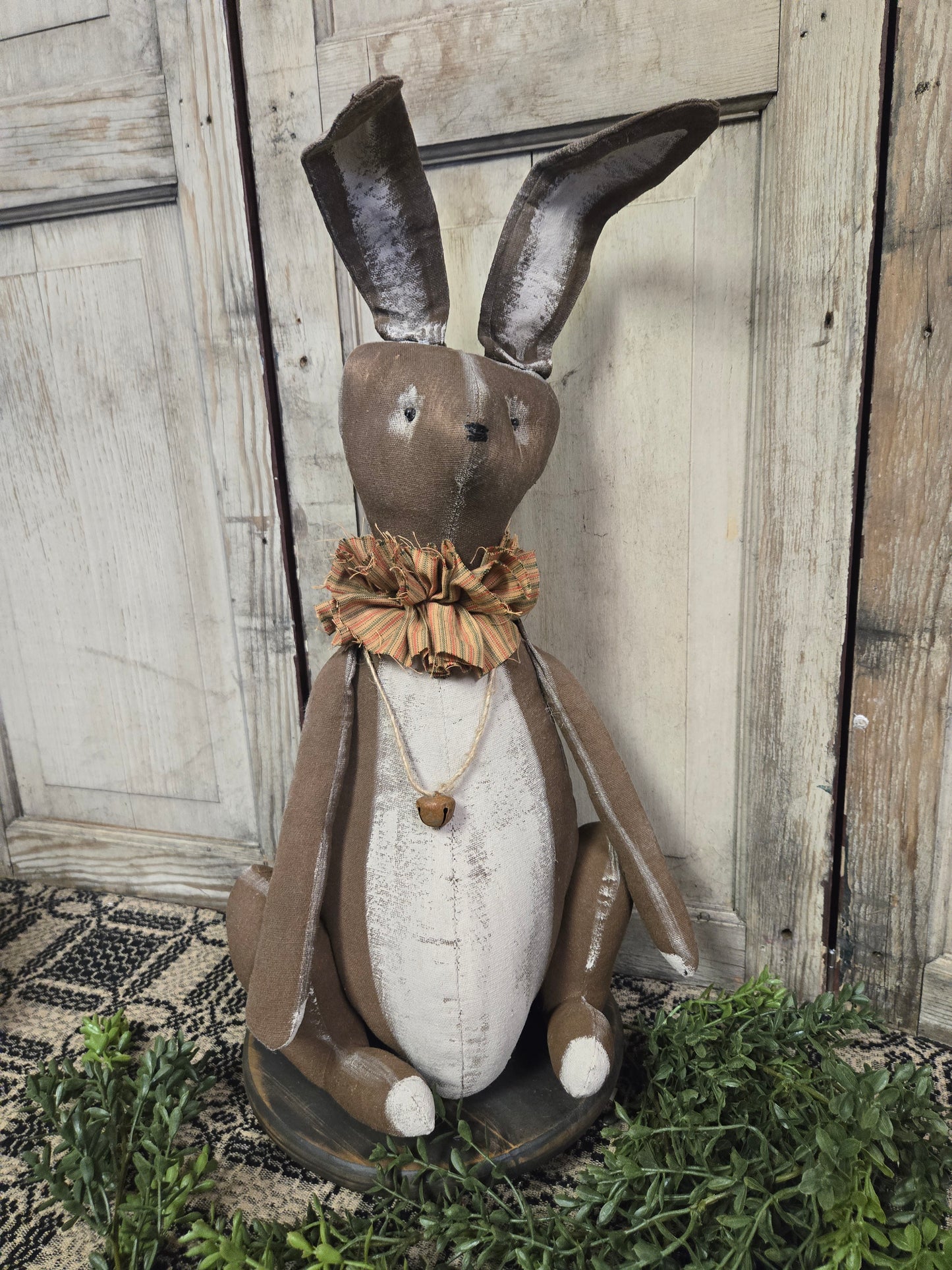 A hand-crafted wooden bunny sculpture with a metal bow and a decorative heart, positioned against a rustic wooden backdrop.