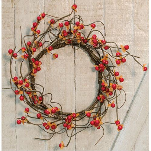 A round wreath made of brown twigs with burnt orange berries and yellow accents, hanging against a wooden background.