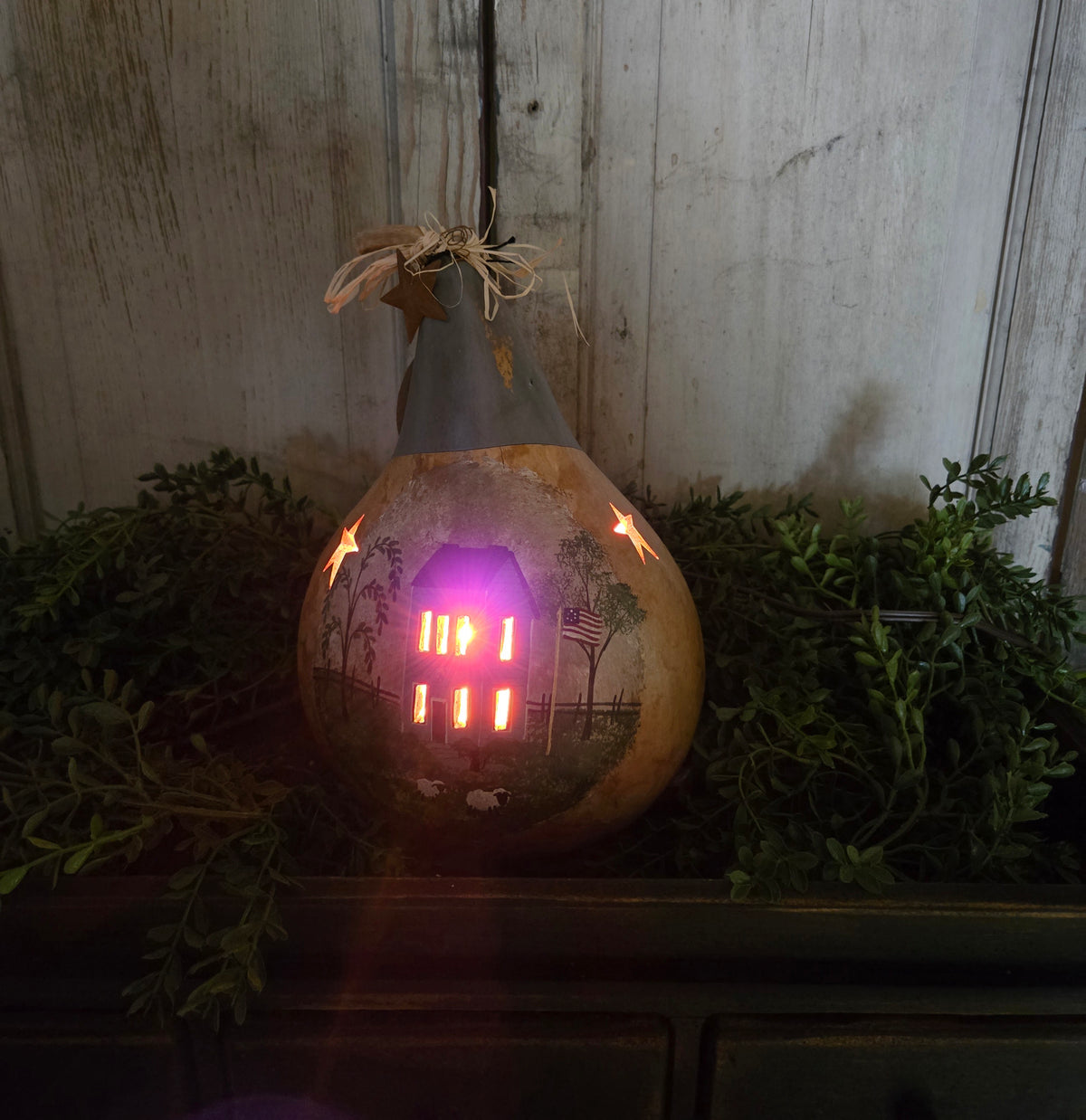 Lighted, carved gourd on a bed of greenery.