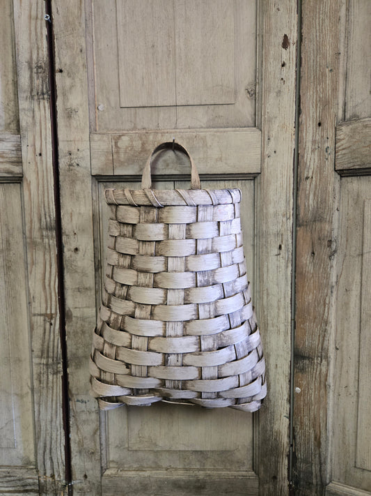 A beige woven basket hanging on a wooden door
