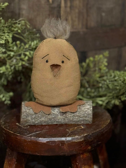 A handcrafted primitive style brown chick with a beige belly sitting on a wooden log.