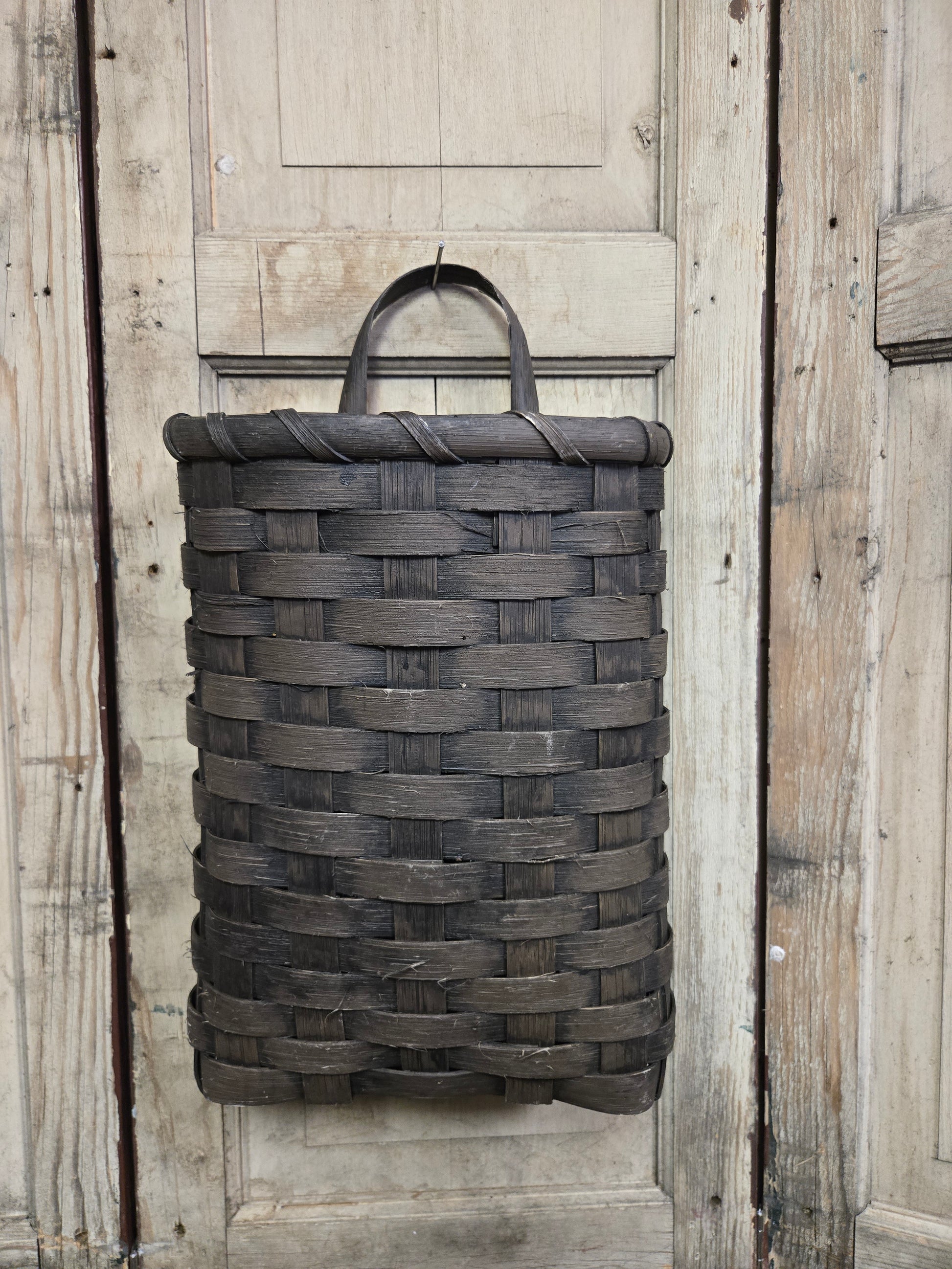 A handcrafted black door basket with a rustic design, hanging on a wooden door.