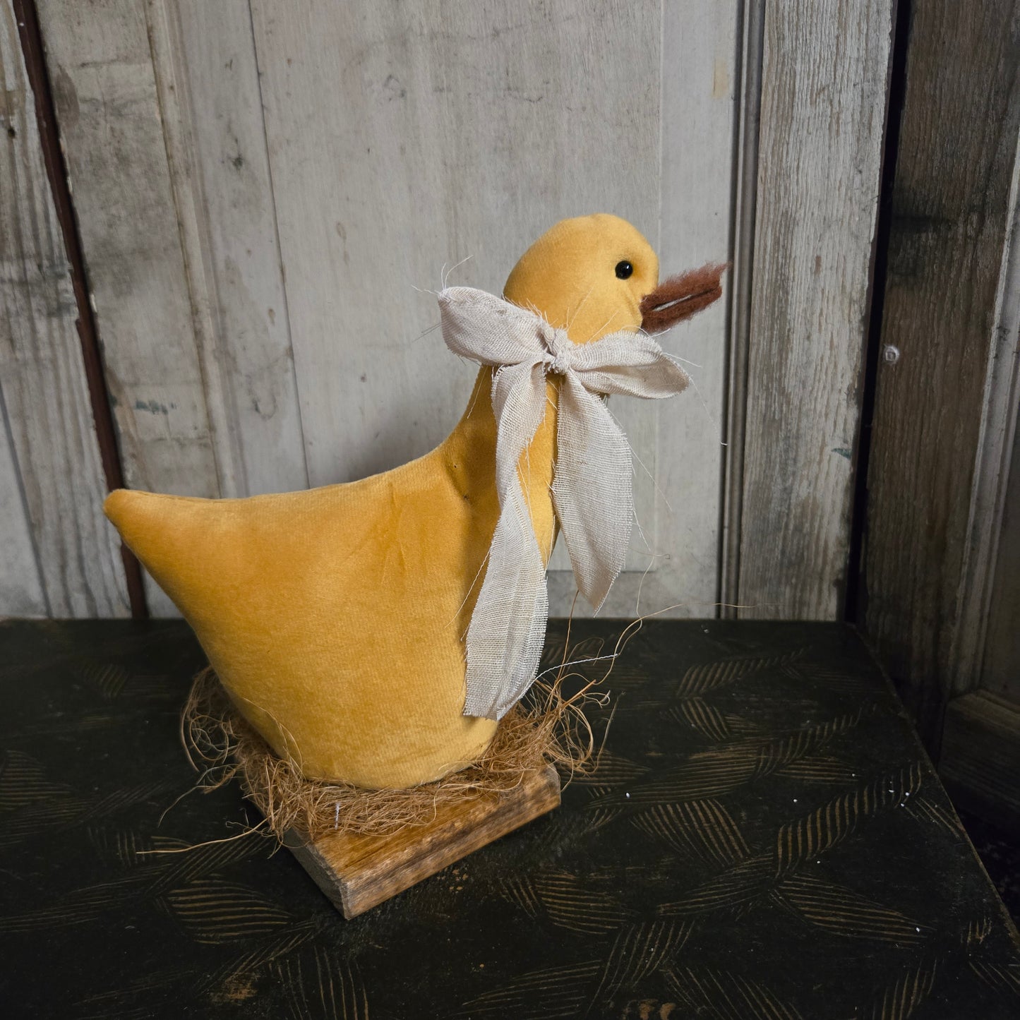Yellow plush duck with a white bow on a wooden surface