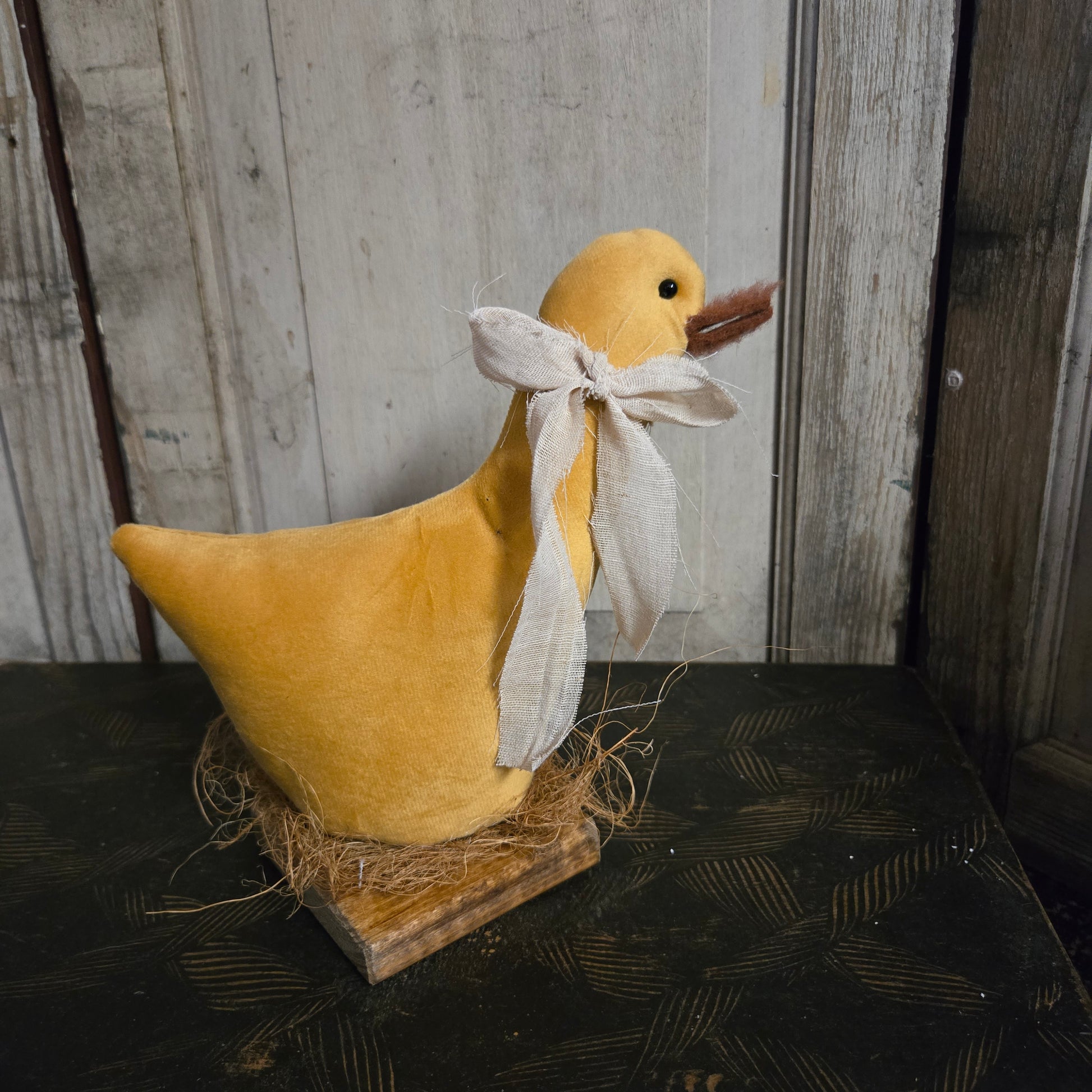 Yellow plush duck with a white bow on a wooden surface