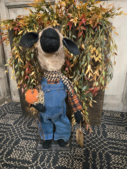 Decorative wreath with a fabric sheep figure, plaid scarf, and pumpkin on a textured surface.
