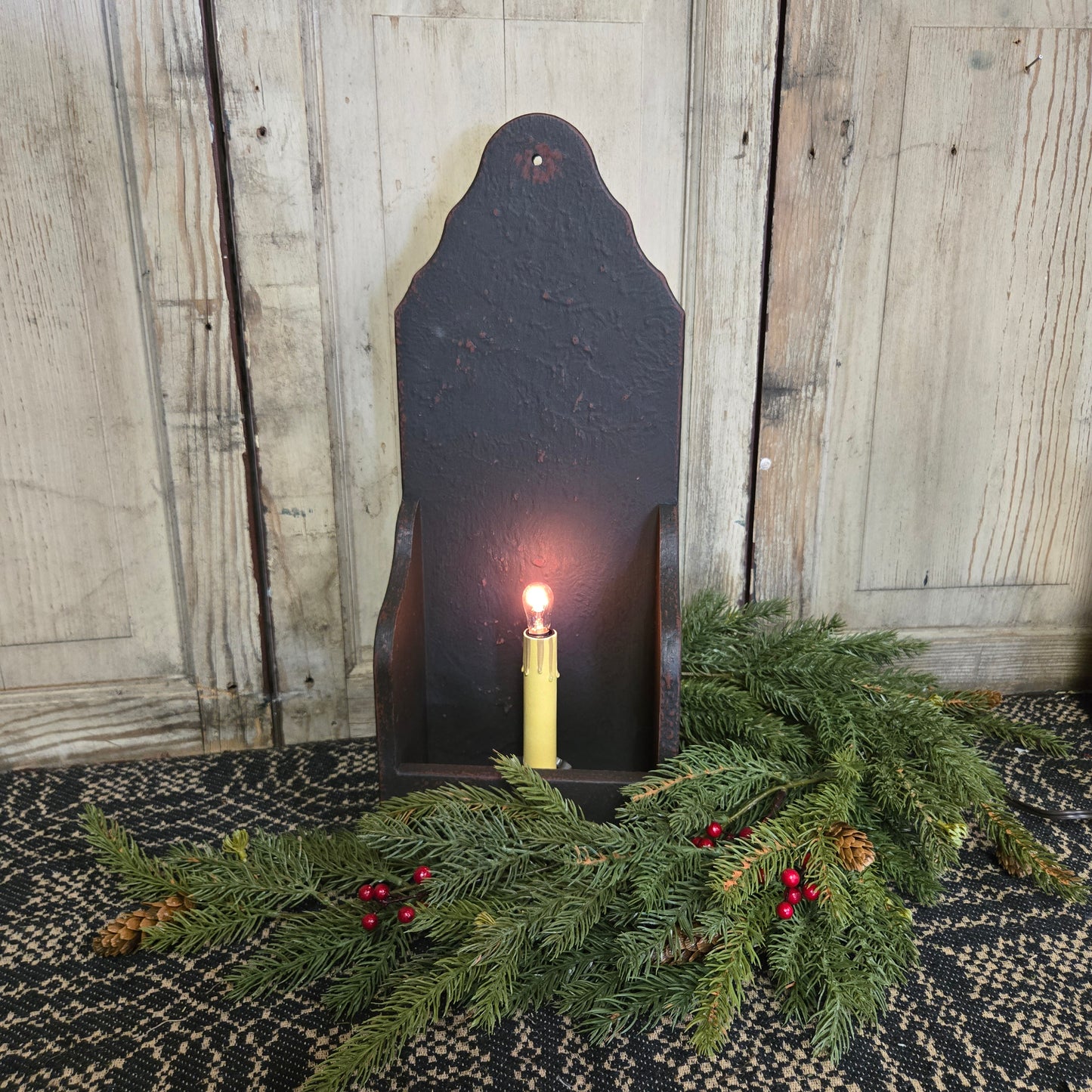 A black wooden electric candle holder with an electric candlestick inside, surrounded by decorative greenery.