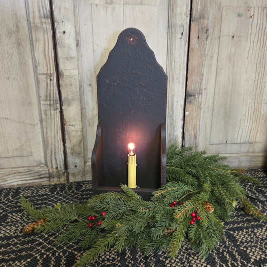 A black wooden electric candle holder with an electric candlestick inside, surrounded by decorative greenery.