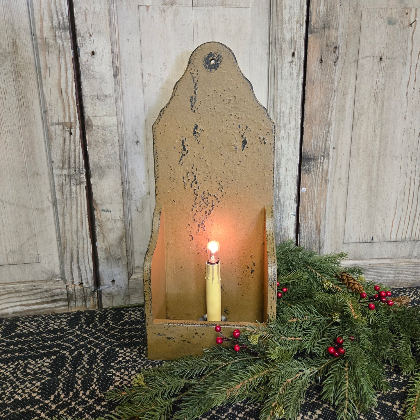 A rustic, mustard-colored wooden candle holder designed for an electric candlestick, displayed with a lit candlestick inside it, surrounded by decorative greenery.