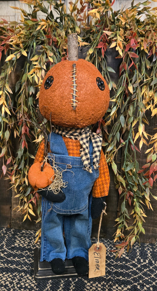 Pumpkin figure with pumpkin head and overalls, surrounded by autumn leaves.