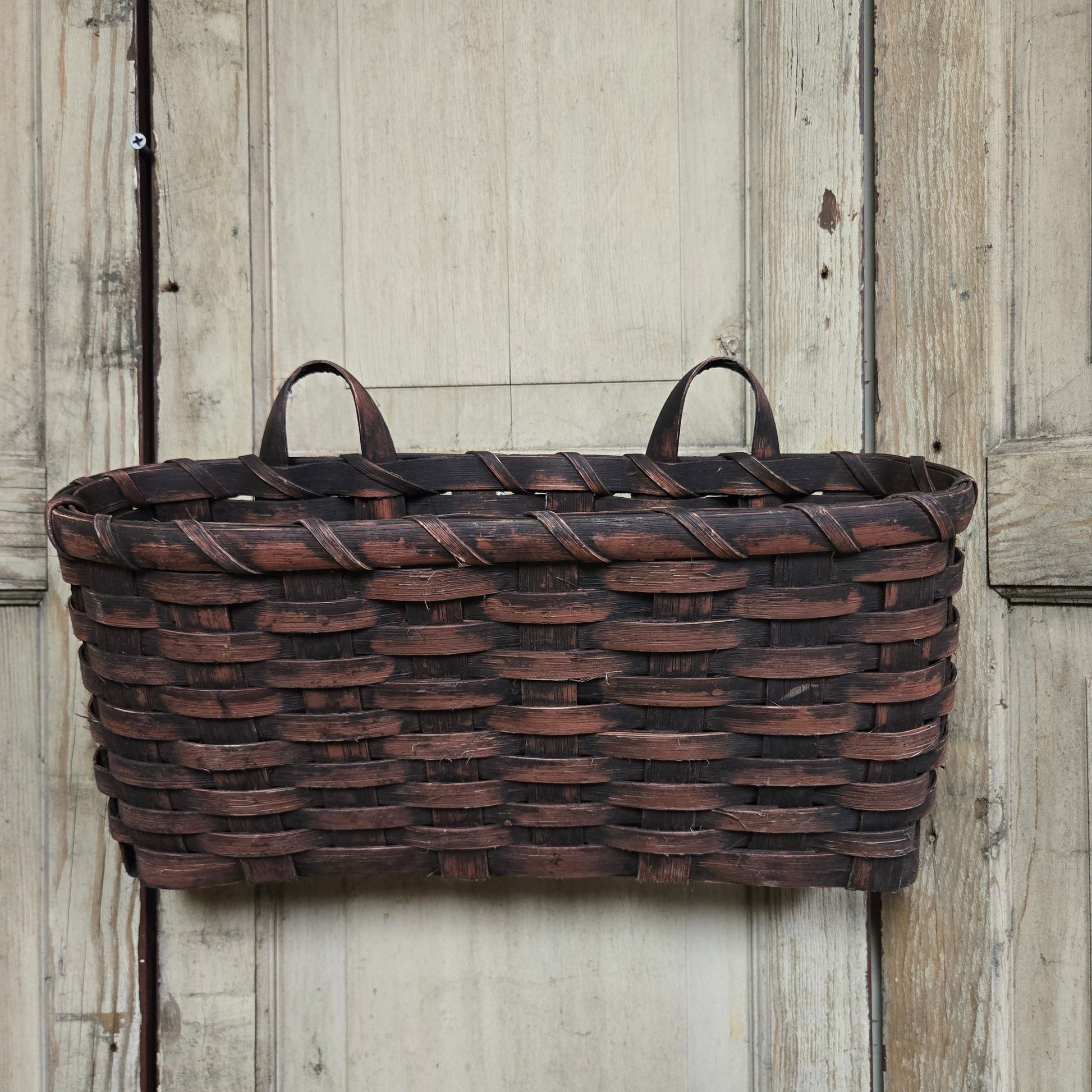 A burgundy wicker basket with handles, on a wooden wall.