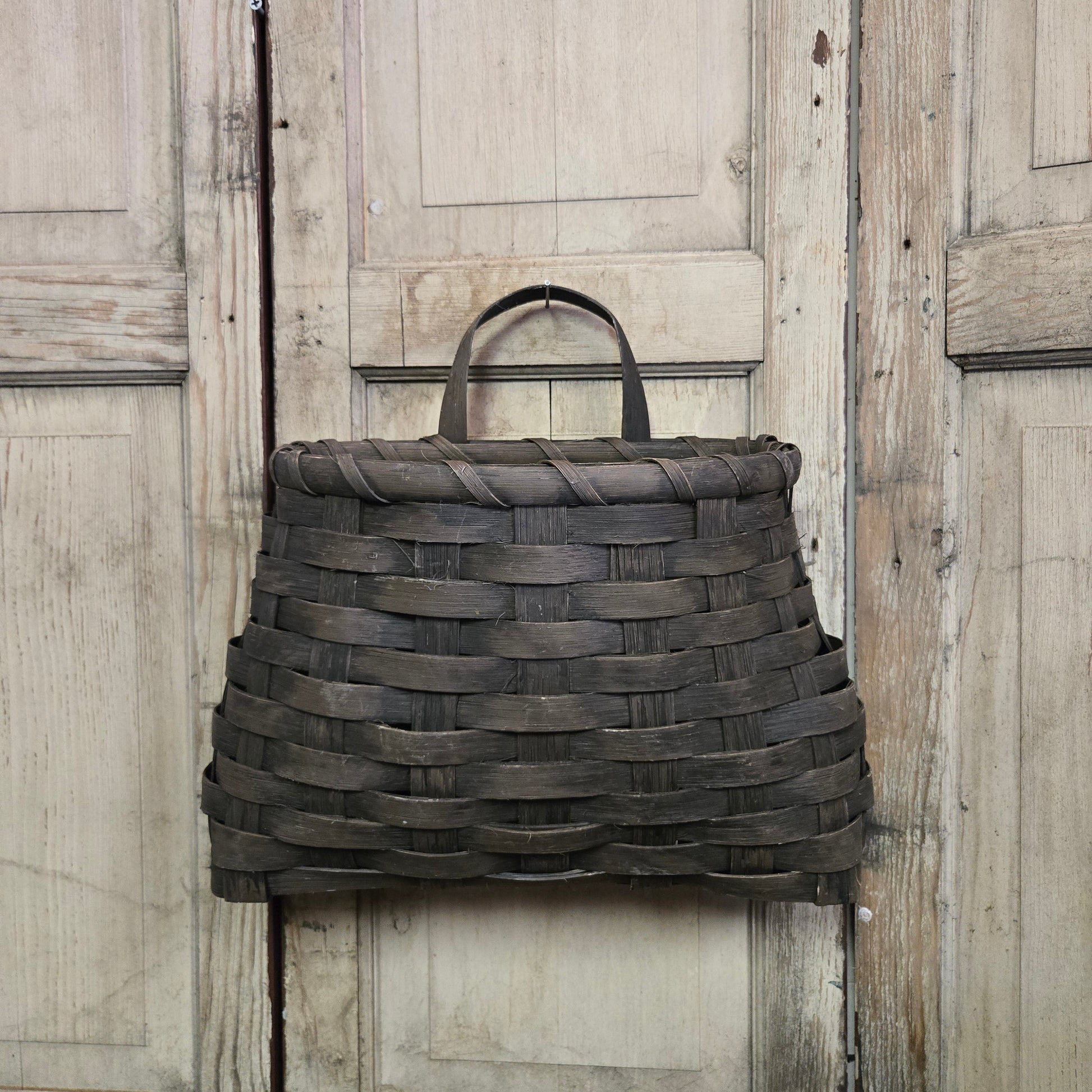 A large black woven wall basket hanging on a wooden door.