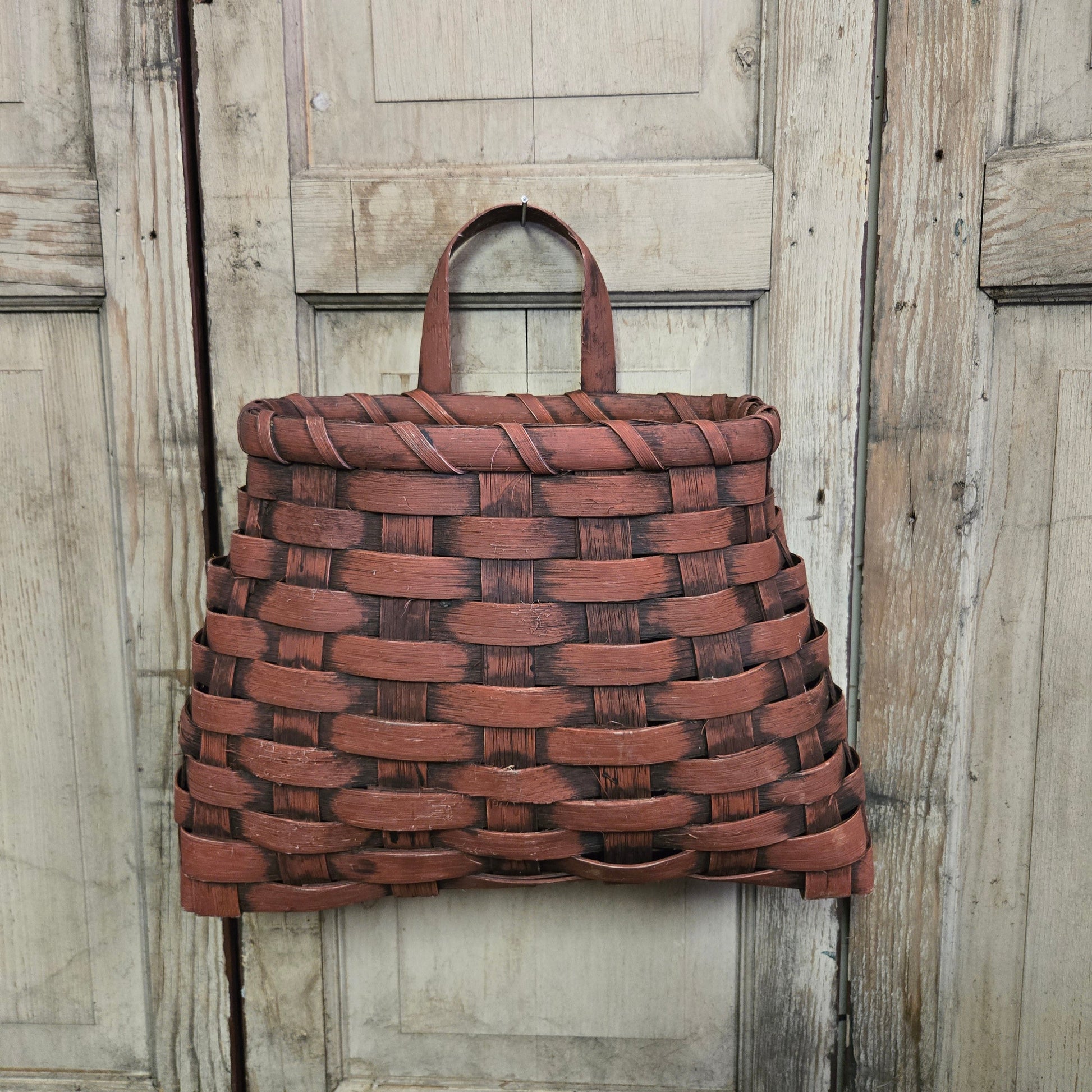 A large burgundy woven wall basket hanging against a wooden background.