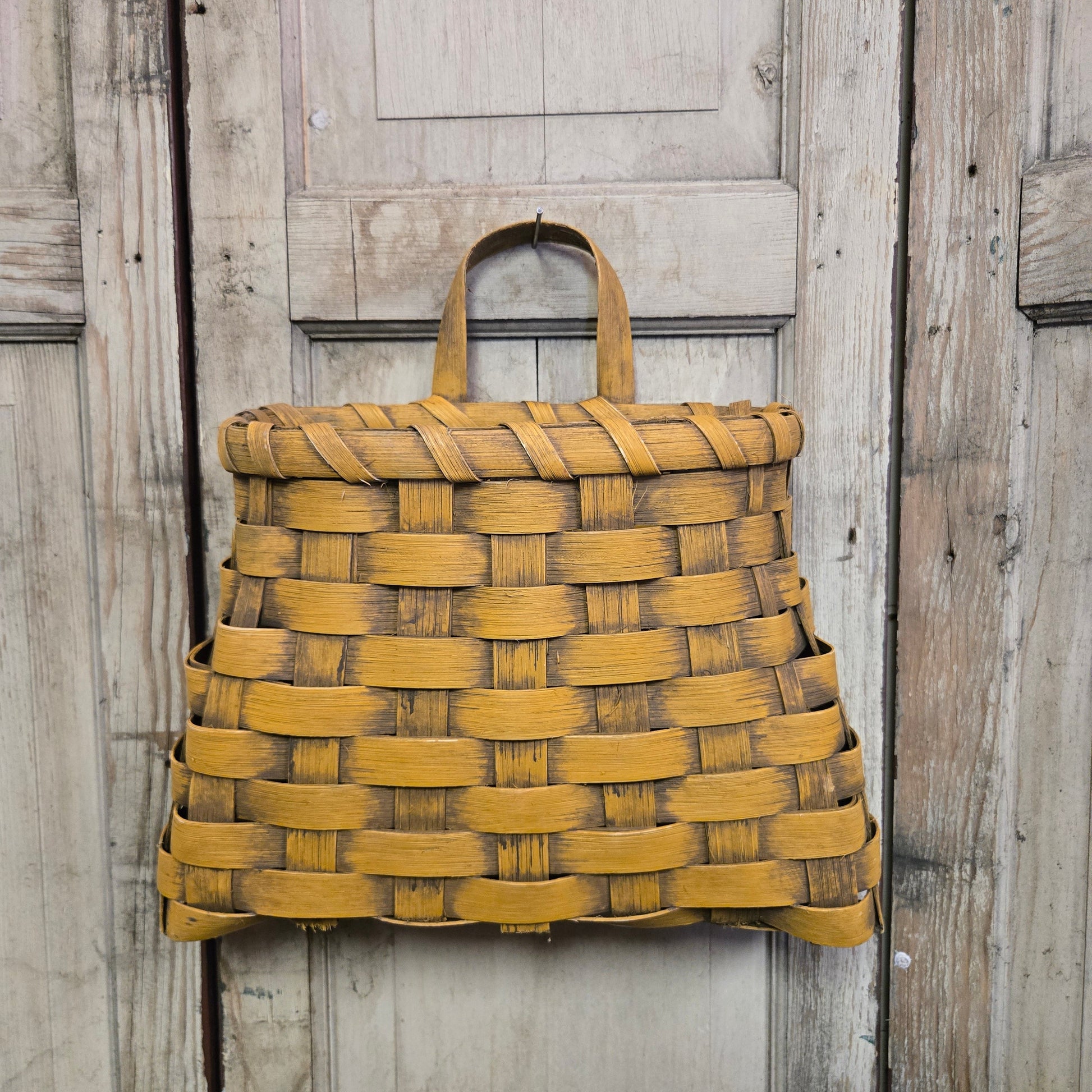 A large mustard-colored woven wall basket hanging against a wooden background.