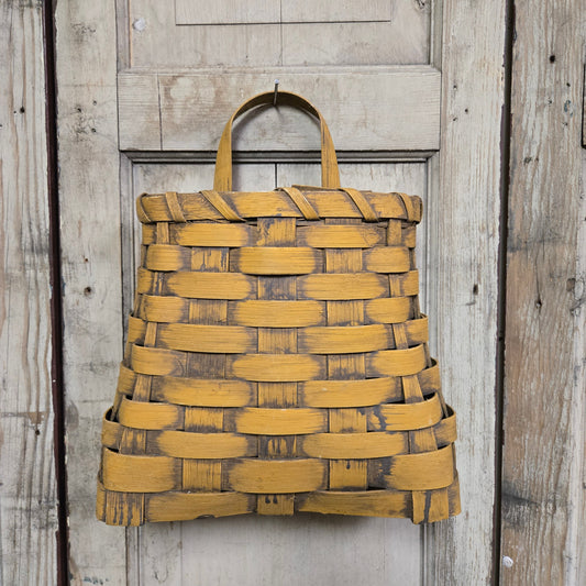 A small mustard-colored woven wall basket hanging on a wooden door.