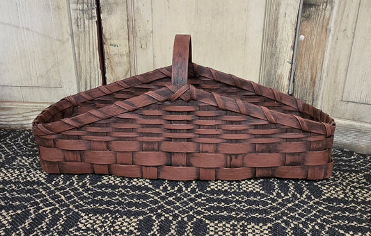 A burgundy, woven basket with a triangular shape, likely used for storing firewood or household items.