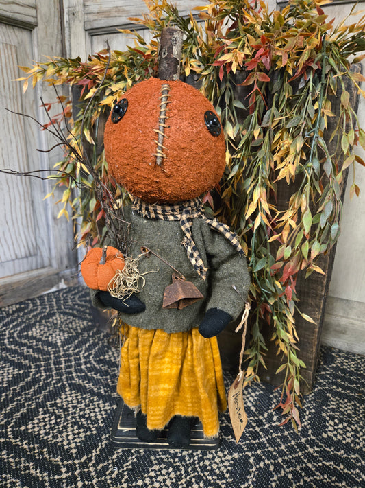 Decorative scarecrow with pumpkin head and autumn leaves on a textured surface