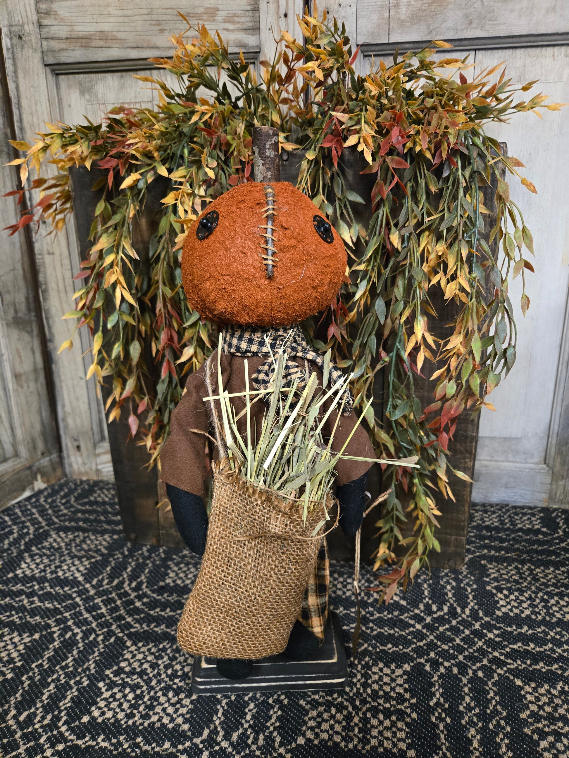 Decorative pumpkin doll  with burlap sack in front of Fall greenery