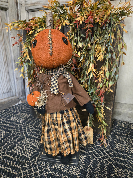 Decorative arrangement with a Pumpkin Doll and foliage on a textured surface.