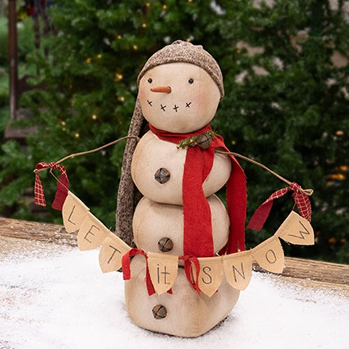 Primitive snowman doll with a knit cap, red scarf, jingle bell buttons, and a ‘Let It Snow’ banner, displayed outdoors in snow