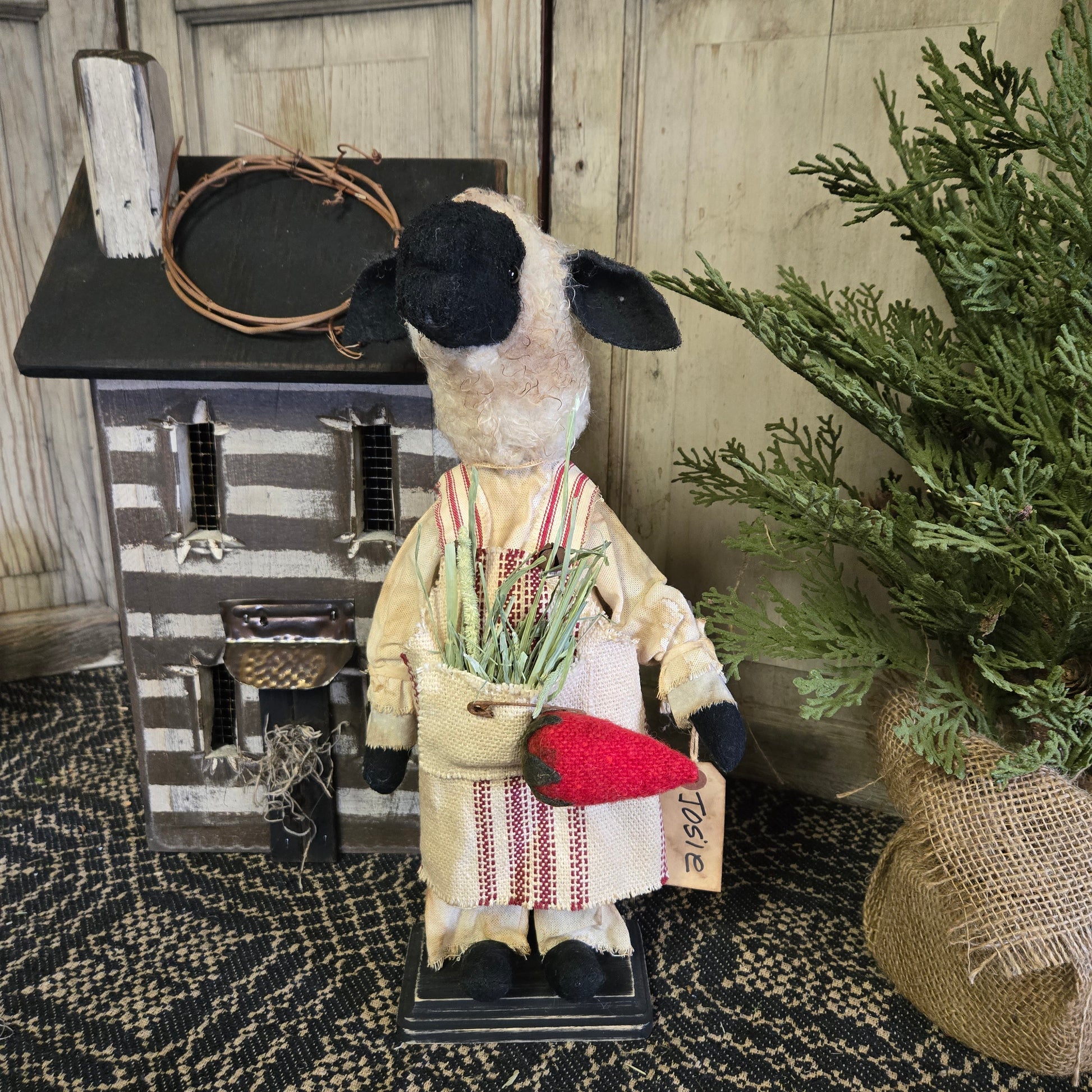 A decorative figurine of a sheep dressed in a costume holding a strawberry, placed near a rustic decorative item and a green plant.