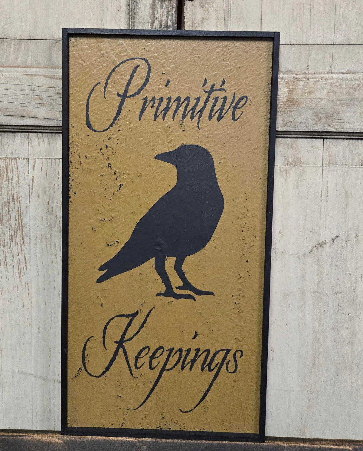 Decorative sign with crow silhouette and 'Primitive Keepings' text on a wooden background