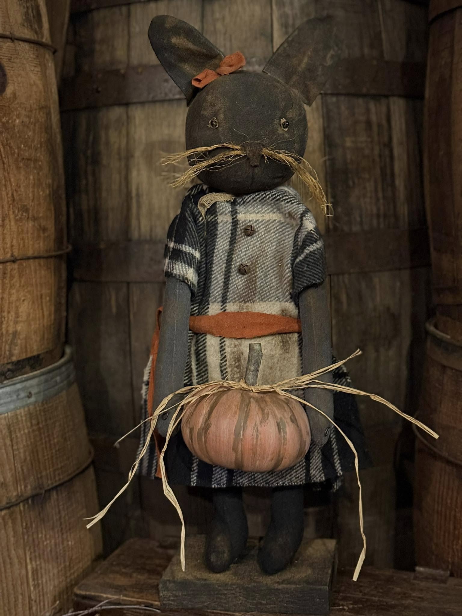 Decorative figure of a cat with a pumpkin, wearing a coat, against a wooden background.