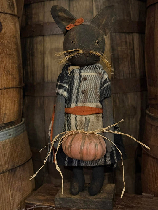Decorative figure of a cat with a pumpkin, wearing a coat, against a wooden background.