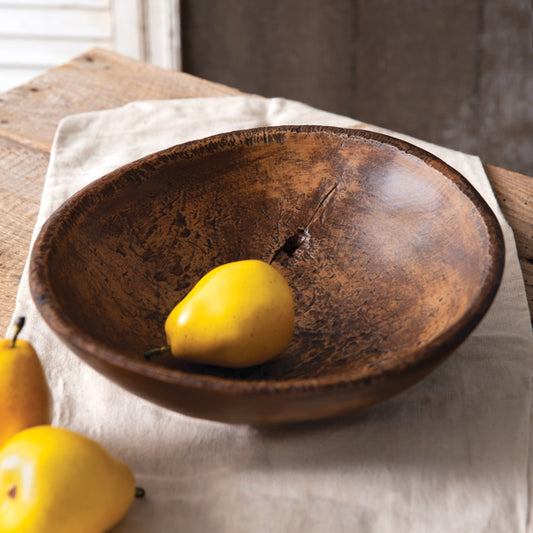 A brown, round, resin bowl with a knot knot in the center creating a hole, displayed on a table with a few pears beside it.