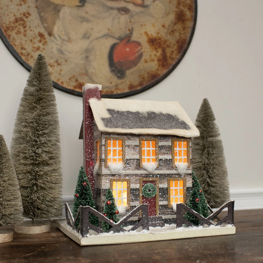 Decorative miniature house with glowing lights in a festive setting with candles and Christmas decorations.