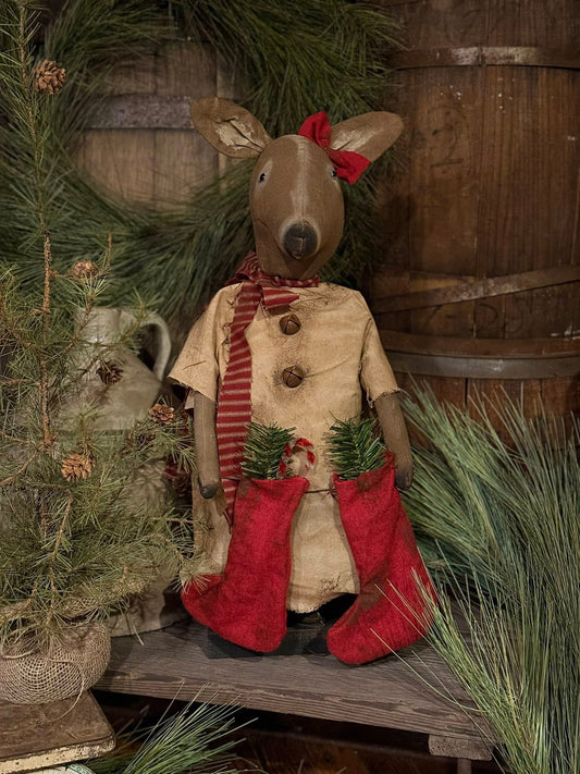 Decorative figure of a reindeer in a rustic setting with barrels and greenery
