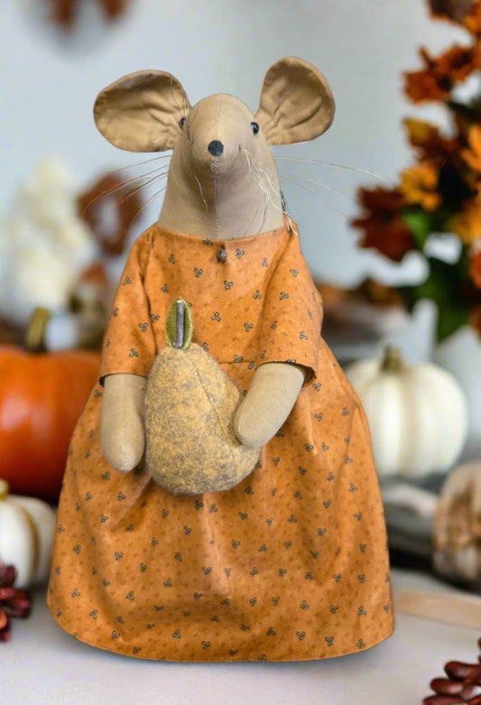Stuffed mouse toy in an orange dress holding a green pear against a wooden background