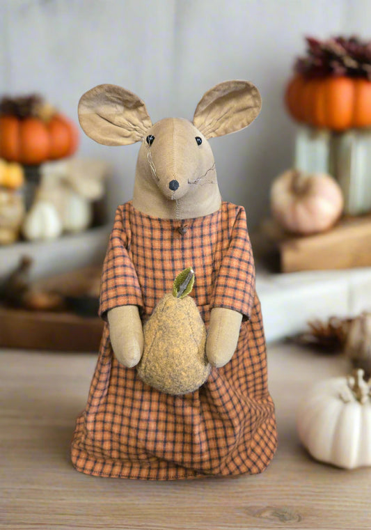 Stuffed mouse in an orange checkered dress holding a pear, with pumpkins in the background.