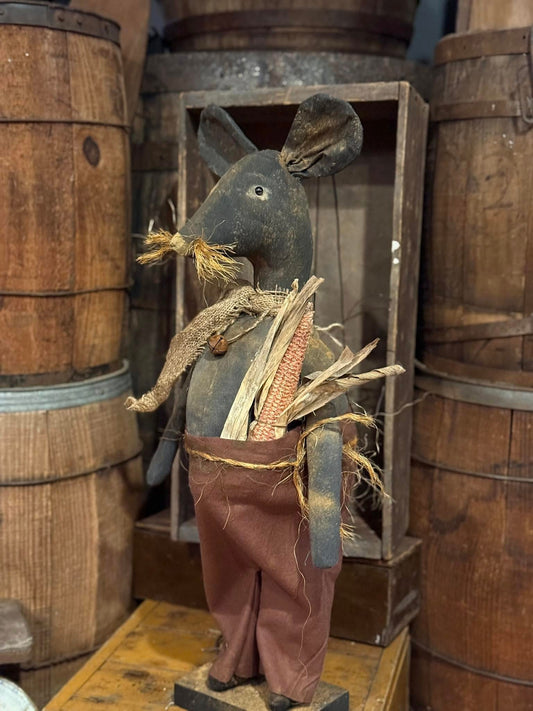 Vintage-style toy mouse with corn in a rustic setting with wooden barrels and crates.