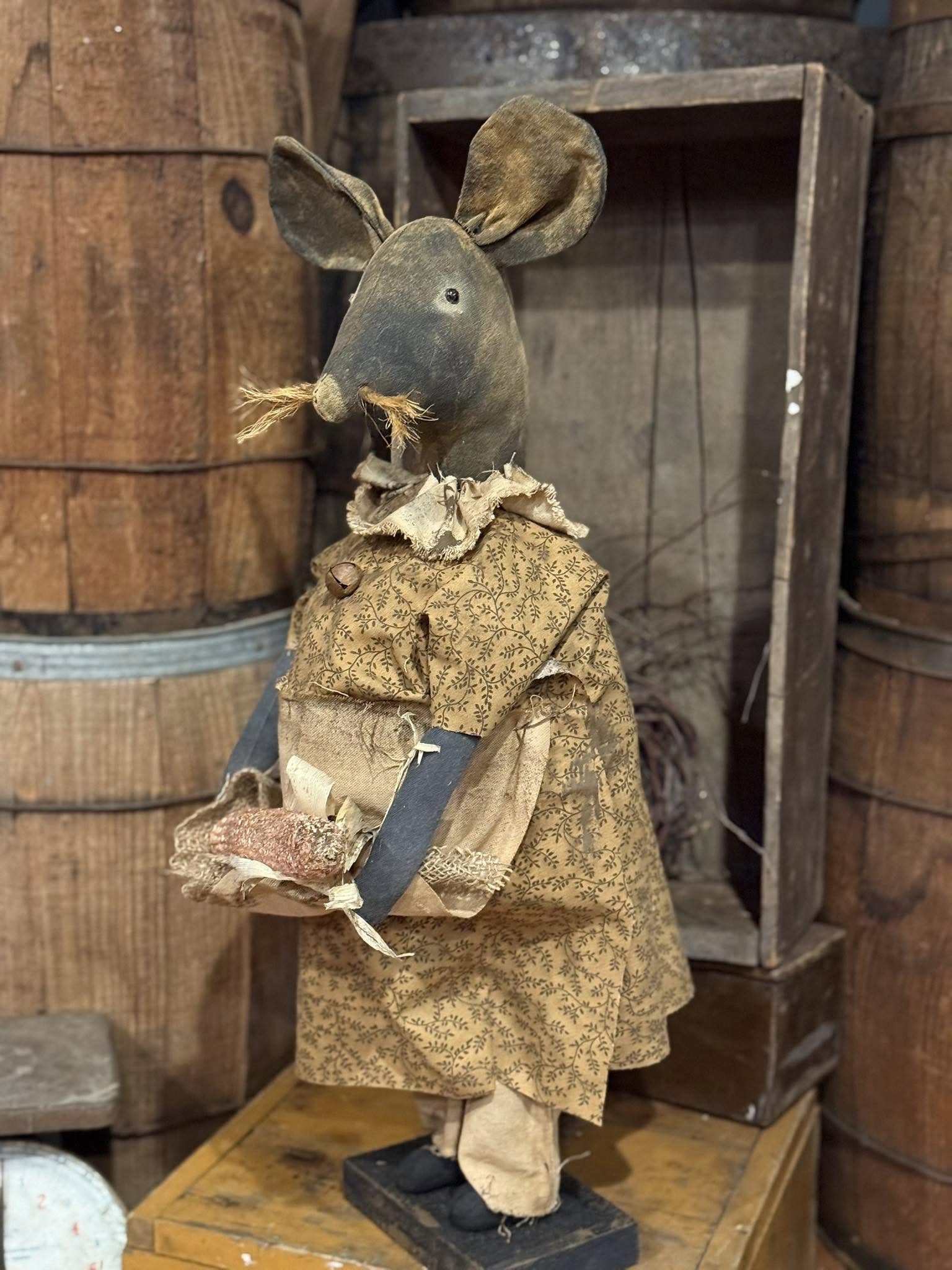 Vintage mouse figure in a rustic setting with wooden barrels and crates.