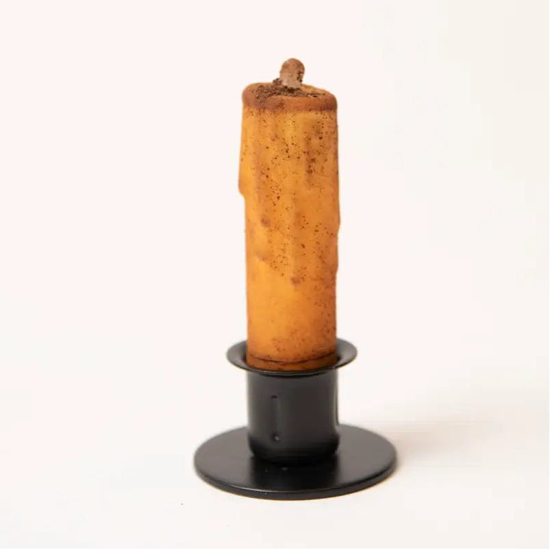 A single rustic, melted wax candle in a black metal holder, photographed against a seamless white background.