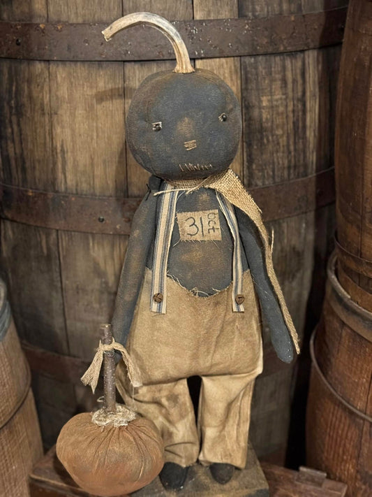 Vintage-style rag doll with a pumpkin head and body against wooden barrels.