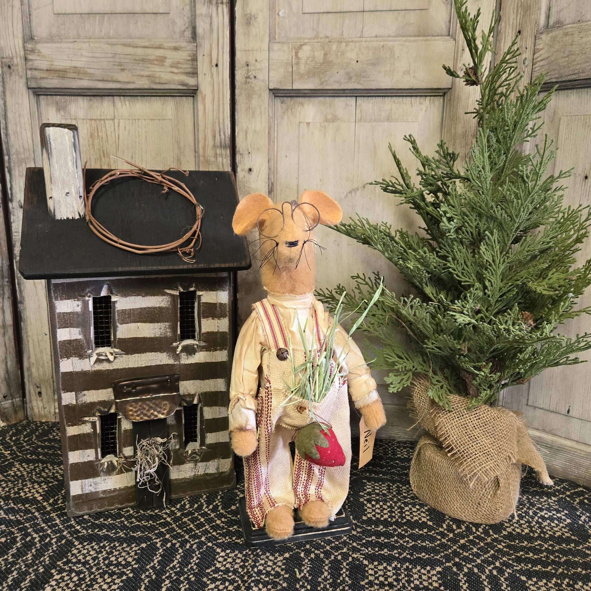 A handcrafted toy mouse with a strawberry accessory, dressed in a costume, standing beside a decorative house and a miniature basket.