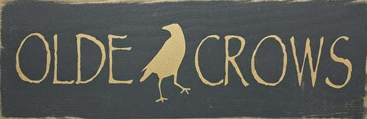 Decorative sign with 'Olde Crows' and a bird silhouette on a wooden surface with foliage.