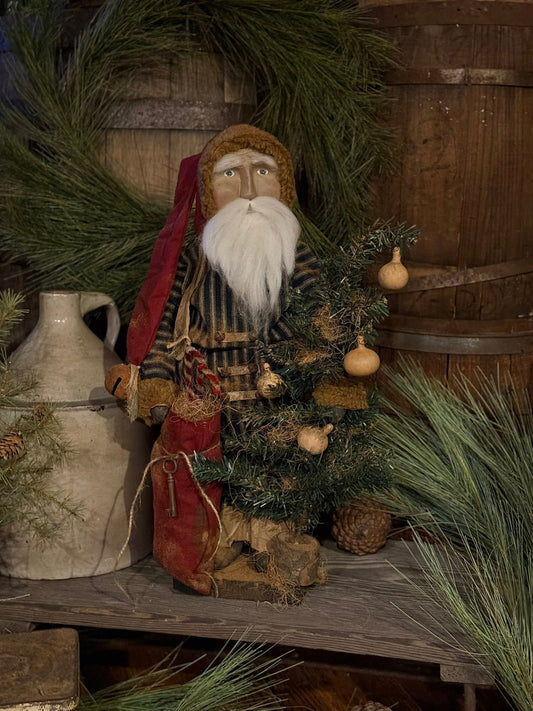 Decorative scene with a rustic Santa figure, small tree, and wreath against a wooden background.