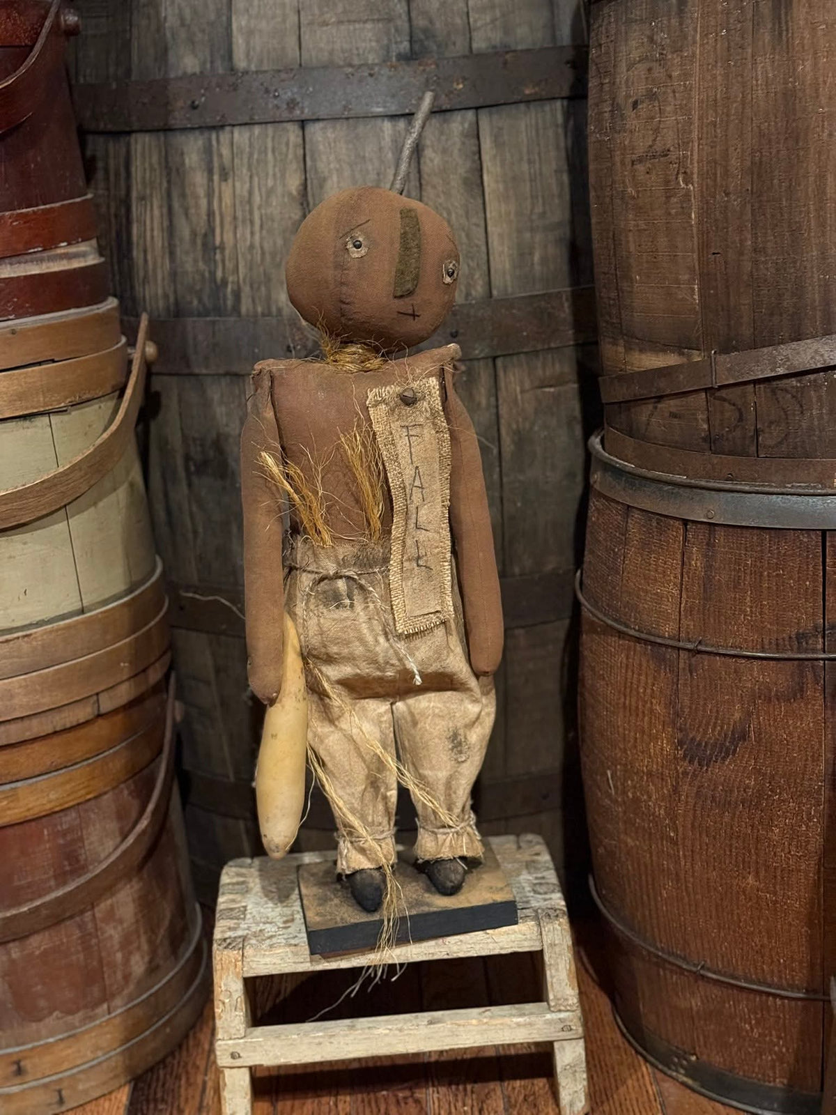 Vintage rag doll in overalls standing on a stool with wooden barrels in the background