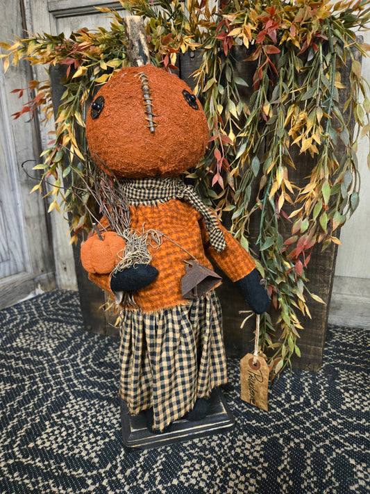 Decorative autumn-themed arrangement with Pumpkin Doll and foliage on a textured surface.