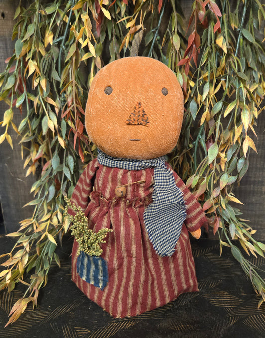 Vintage-style doll with a striped dress and checkered scarf against a leafy background
