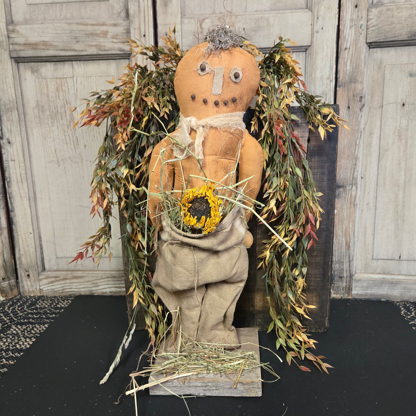 Decorative pumpkin doll with dried plants and a sunflower against a wooden background.