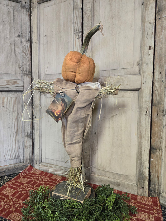 Wooden scarecrow with fabric pumpkin head standing in front of a white wood door.