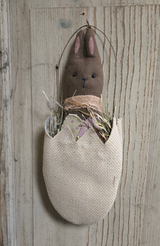 Textile rabbit decoration in a woven egg on a wooden background