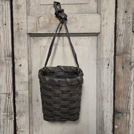 A brown woven basket hanging on a door knob.