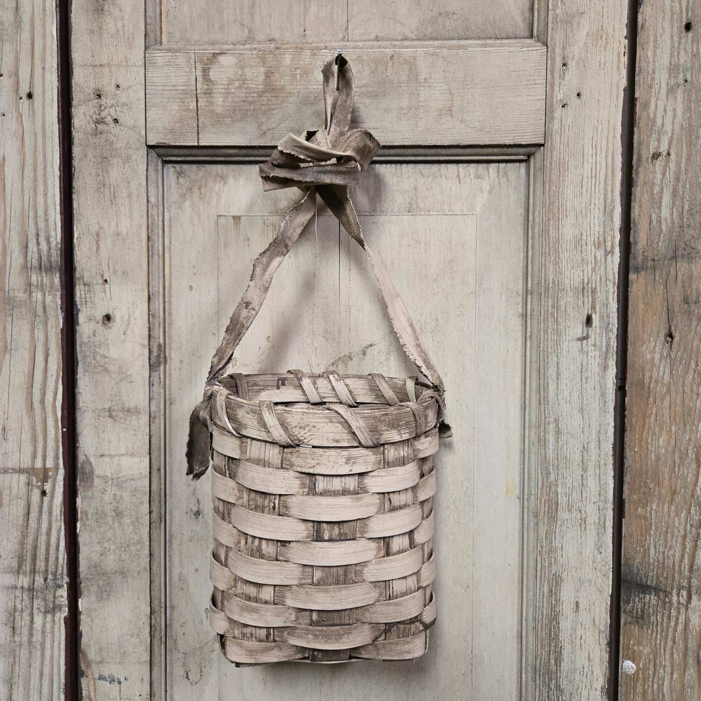 A beige woven basket hanging against a wooden background.