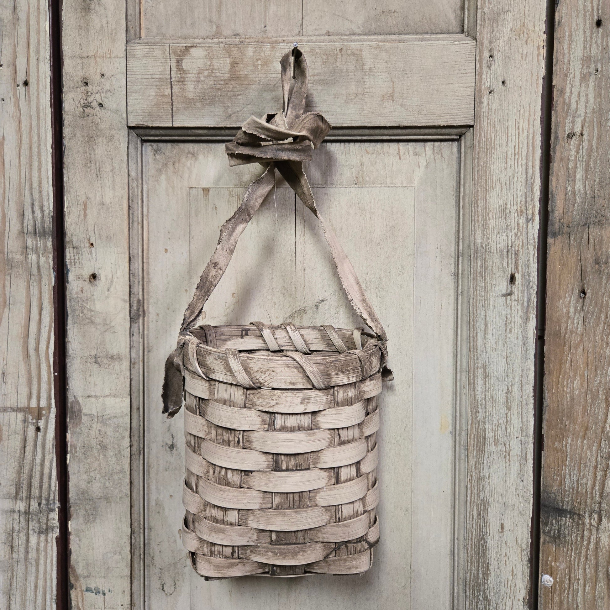 A beige woven basket hanging against a wooden background.