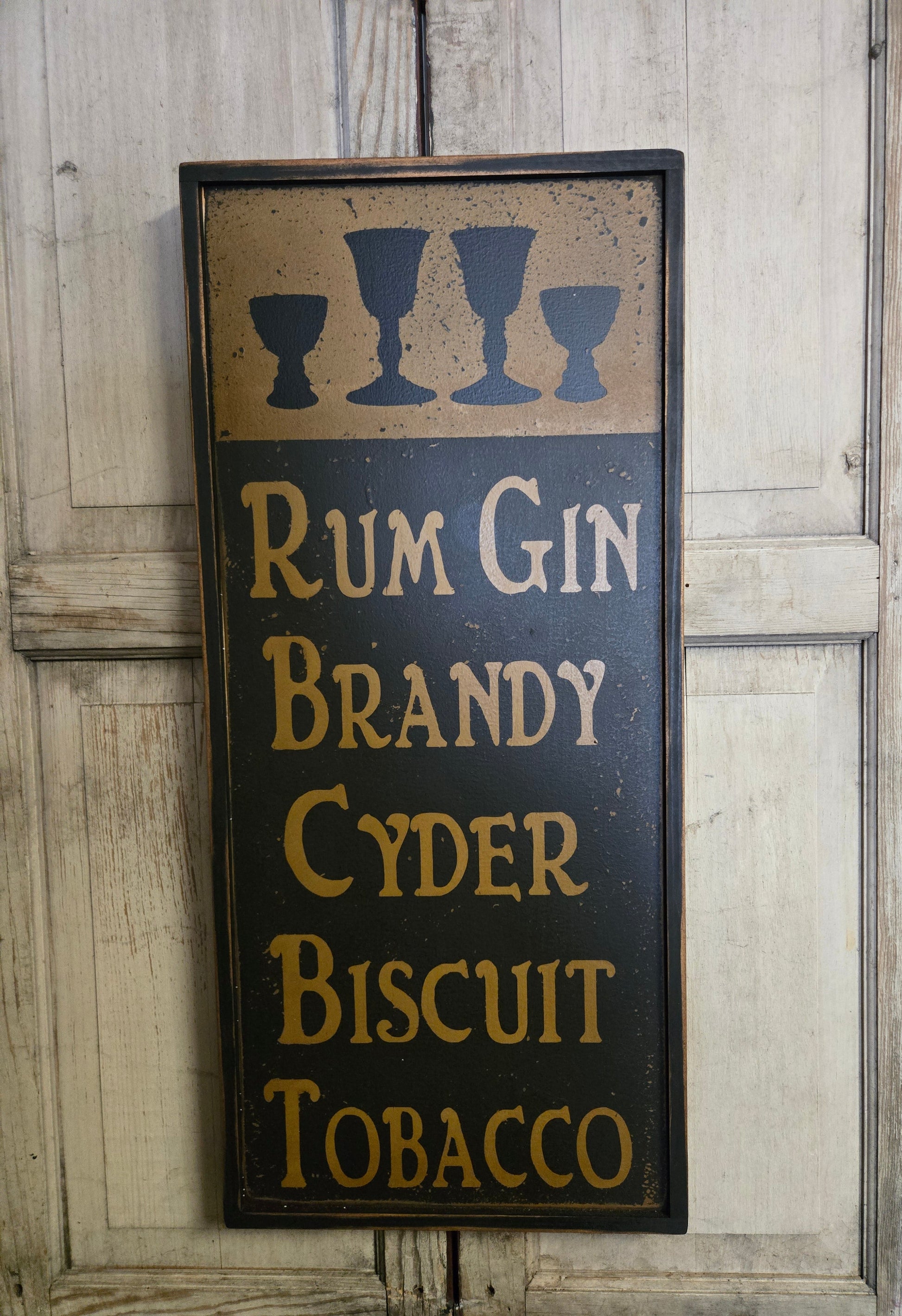 Decorative sign with text 'Rum Gin Brandy Cyder Biscuit Tobacco' on a wooden background
