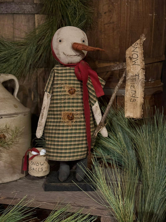 Decorative snowman figurine with plaid dress and red scarf in a rustic setting.